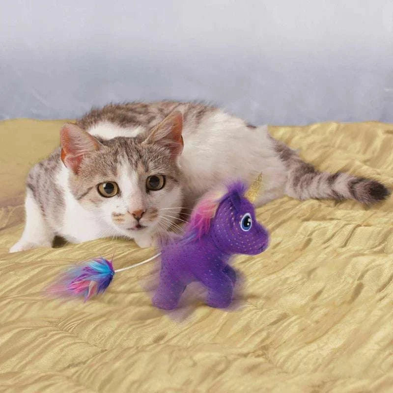 Cat playing with KONG Enchanted Buzzy Unicorn Cat Toy on a bed.