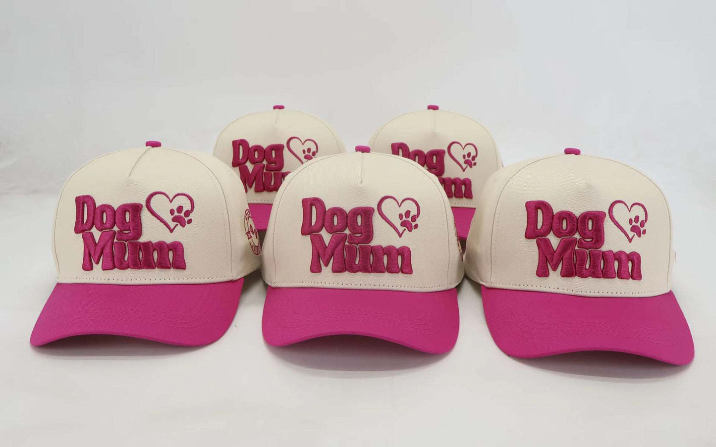 Beige and pink embroidered Dog Mum baseball hats displayed in a group