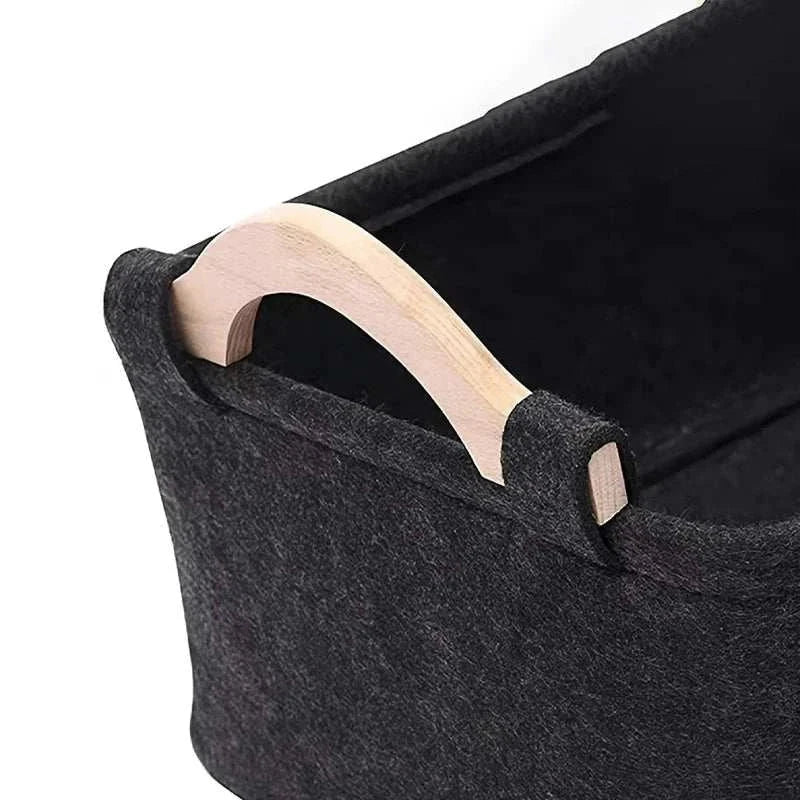 Black felt pet toy storage basket with wooden handles for organizing and storing dog toys.