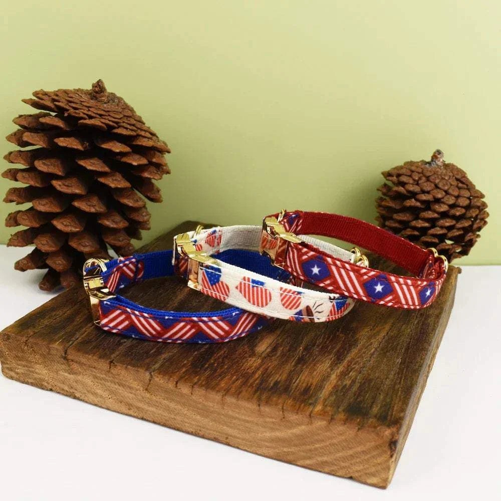 Personalised cat collars with adjustable soft fabric and patriotic bow design, displayed on wooden block with pinecones