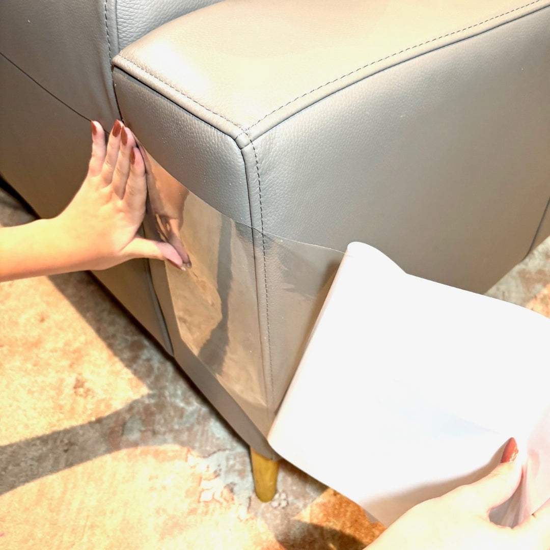 Hands applying transparent Cat V’s Couch Defender scratch deterrent tape on beige couch corner for cat furniture protection