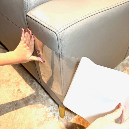 Hands applying transparent Cat V’s Couch Defender scratch deterrent tape on beige couch corner for cat furniture protection