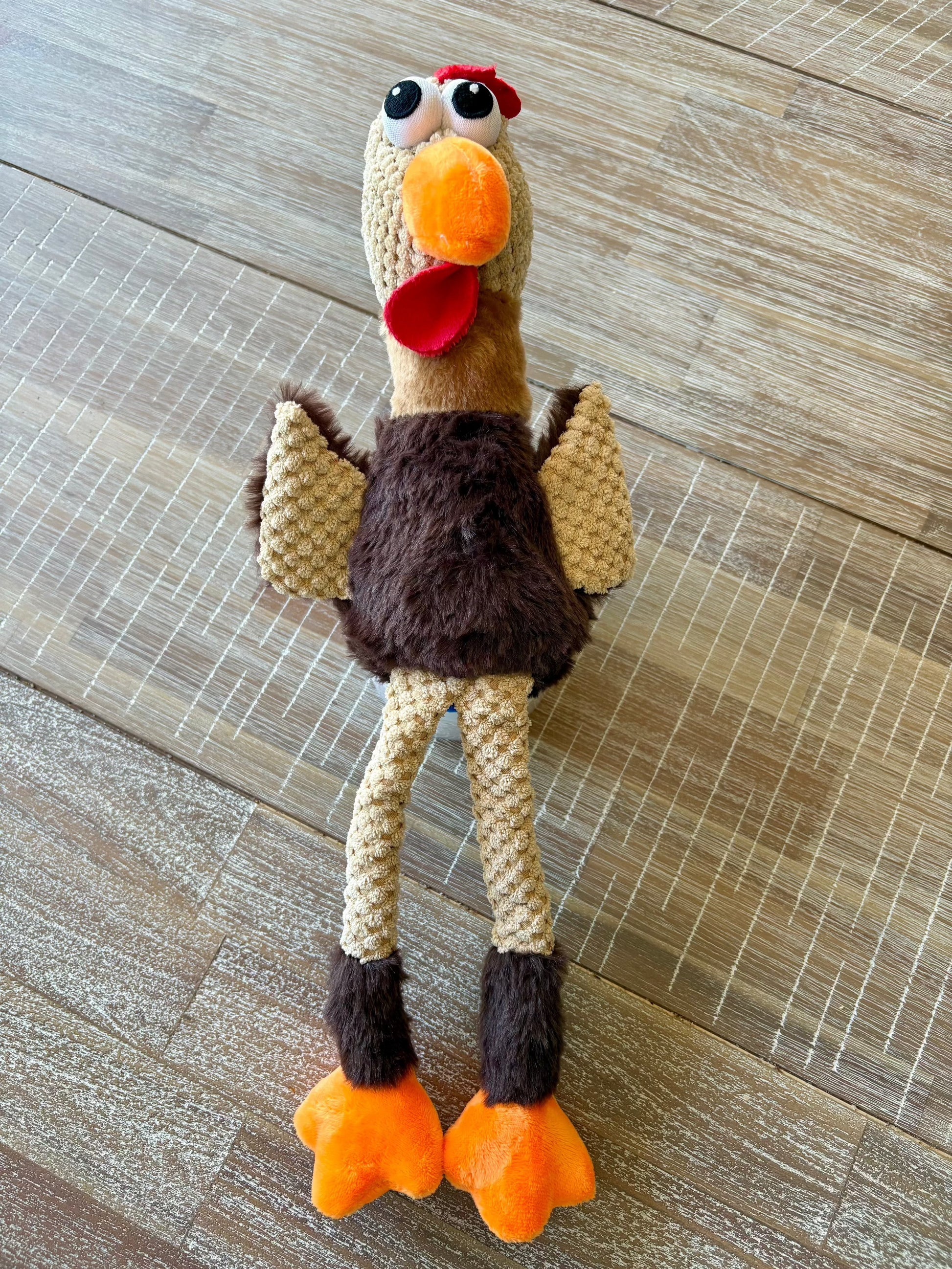 Plush squeaky chicken dog toy on wooden floor.