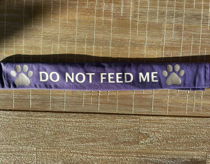 Purple cotton lead slip for dogs with "DO NOT FEED ME" text and paw prints, designed for safety and communication.