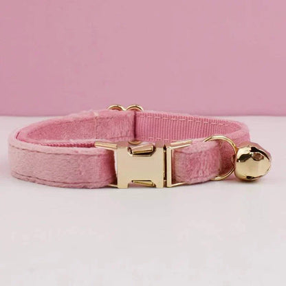 Pink luxury velvet cat collar with gold buckle and bell on a white surface