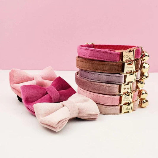 Stack of luxury velvet cat collars with personalized engraved nameplates, bells, and matching velvet bow ties in various pink and mauve shades