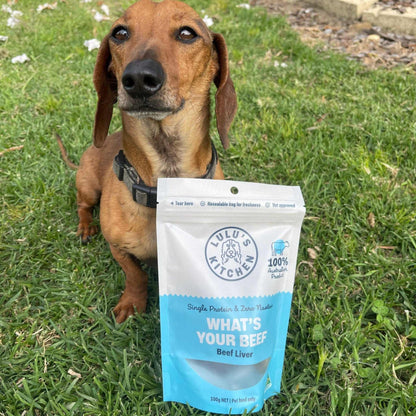 Dog with "What's Your Beef? - Beef Liver" treat bag on grass, 100% Australian, nutritious training treat.